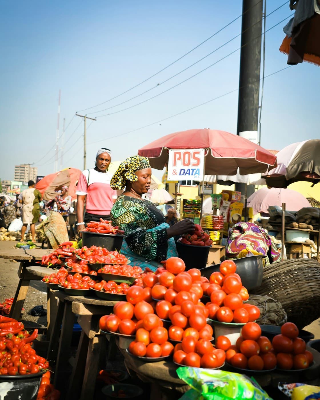 A trader at her market stall, tomatoes and peppers laid out in front of her