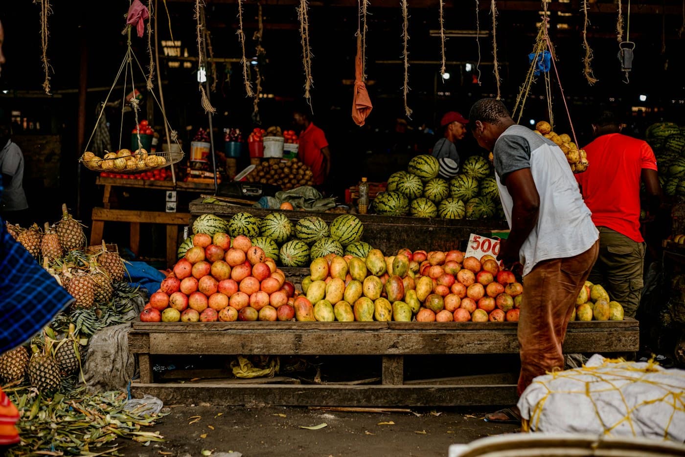 A fruit seller arranging a price card over mangoes and watermelons